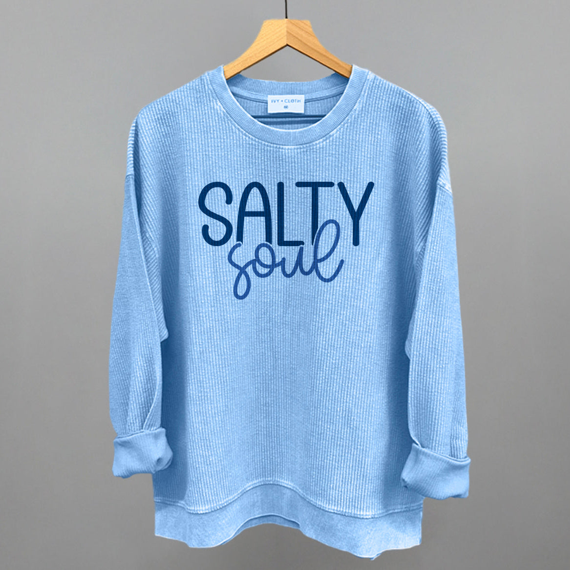 Blue sweatshirt with 'Salty Soul' text on a hanger against a gray background